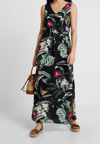 Vestido maxi floral en negro, con flores rosas y blancas, patrones de hojas, diseño de escote en v, cintura ceñida y aberturas laterales.