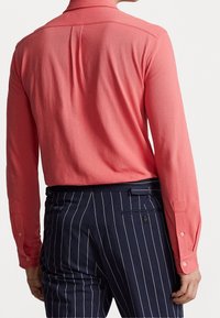 Košile s dlouhým rukávem z korálové látky, hladký povrch, s límečkem a manžetami na knoflíky. Spárovaná s kalhotami s námořnickým proužkem a zadními kapsami.