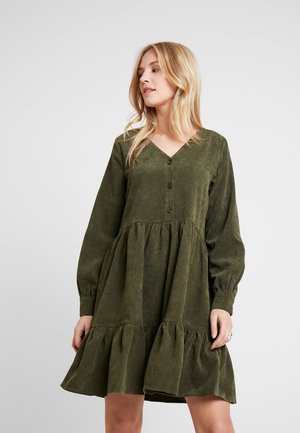 Robe vert olive, décolletée en V, avec des manches longues, des détails de boutons et un ourlet en bas à volants. Fabriquée dans un tissu textured doux.