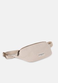 Beige canvas fanny pack with a zippered closure, adjustable strap, and a logo patch. Textured fabric and streamlined, oval shape.