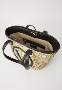 Bolso de paja trenzada con acentos de cuero negro, parte superior abierta y bolsillo interior. Cuenta con asas negras sólidas y un forro beige.