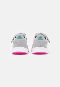 Une paire de baskets Adidas grises avec un logo turquoise au talon, des semelles blanches et des semelles extérieures rose vif, vue de l'arrière.