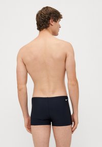 Sötétkék fürdőnadrág, testhezálló kialakítással, rugalmas anyagból, a hátsó derékpánton egy kis fehér Nike logóval.