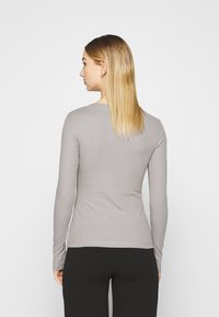 Long-sleeve ribbed top in light gray, featuring a fitted design and crew neck, with smooth fabric and a subtle texture.