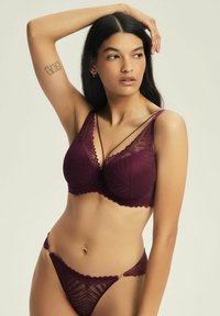 Bordowy koronkowy stanik z dekoltem w serek i falbaniastymi brzegami, z geometrycznym wzorem oraz cienkimi, regulowanymi ramiączkami. W zestawie znajduje się pasujący string.