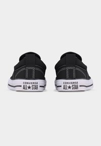 Para czarnych, niskich sneakersów Converse All Star widzianych od tyłu na jednolitym białym tle.