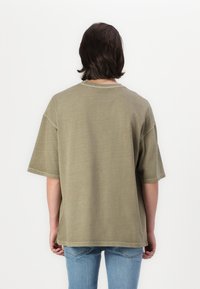 Olivenfarvet oversized t-shirt med korte ærmer, rund halsudskæring og synlige syninger. Bæres med lyseblå jeans.