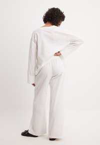 Valge linane pikkade varrukatega särk ja sobivad püksid, millel on lõdva istuvuse, laiad säärted ja selja lõhiku detail.