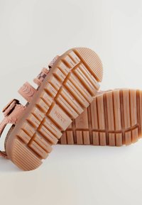 Rosa sandal med texturerade remmar, justerbar spänne och ett mönstrat design. Tjock gummisula med djupa spår för grepp.