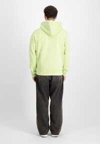 Felpa verde chiaro con cappuccio, polsini e orlo a costine, abbinata a jeans grigi scuri a gamba larga. Design semplice e casual.