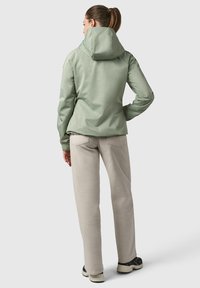 Veste à capuche vert clair avec une finition texturée, des poignets élastiques et une taille ajustable, associée à un pantalon beige et des chaussures noires.