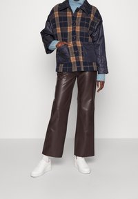 Vadderad rutig jacka i marinblå, brun och gula nyanser, med stora frampocketar, i kombination med bruna läderbyxor med vida ben och vita sneakers.