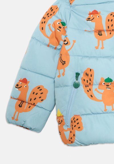 Lyseblå pufferjakke med oransje tegneserieekorn. Har en grønn glidelås og quiltet tekstur. Designene inkluderer lekne uttrykk og eikenøtter.