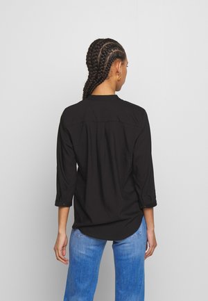 Camicia nera a maniche lunghe con una vestibilità rilassata, dotata di colletto button-down, maniche arrotolabili e una yoke posteriore. Abbinata a jeans blu.