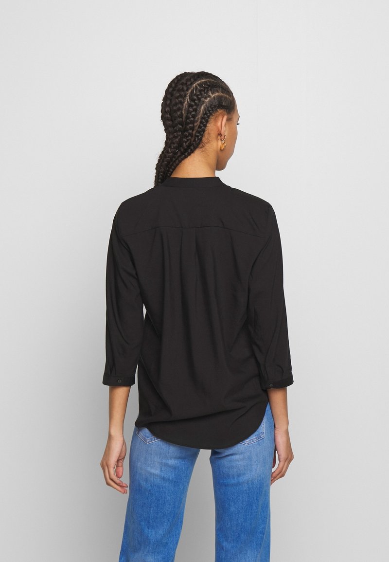 Camicia nera a maniche lunghe con una vestibilità rilassata, dotata di colletto button-down, maniche arrotolabili e una yoke posteriore. Abbinata a jeans blu.