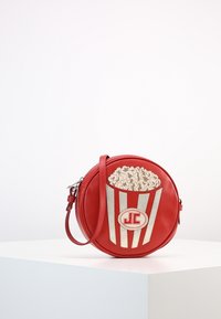 Rund röd läderväska med ett popcornmotiv, vita ränder och beige popcorndetaljer. Inkluderar en avtagbar axelrem.