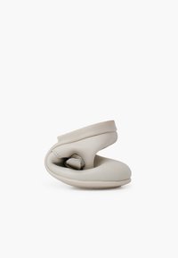 Calzado flexible de color gris claro con forma contorneada, textura suave y suela texturizada. Presenta una correa en la parte superior para ajustar el ajuste.