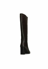 Botte en cuir marron montante avec un design épuré, à bout carré et talon épais. Texture lisse et accents minimalistes. Vue de côté.