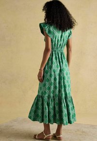 Grünes gemustertes Kleid mit kurzen Rüschensäumen, einem elastischen Bund und einem ausgestellten Saum. Der Stoff wirkt leicht und hat eine strukturierte Oberfläche.