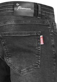 Jeans de mezclilla negra con una textura suave, que presentan un bolsillo trasero prominente y una etiqueta de cuero negro con marca en la cinturilla.