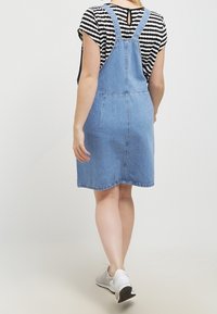 Džínová šaty s laclem, světle modré, ke kolenům, s nastavitelnými ramínky, rovného střihu a se dvěma zadními kapsami. Spárované s proužkovaným topem.
