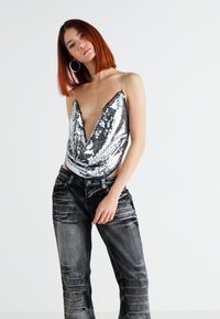 Body in paillettes argento con scollo a V profondo e spalline sottili, abbinato a jeans in denim nero testurizzato a vestibilità rilassata.