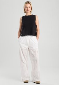 Black knit sleeveless top with side ties paired with white eyelet-pattern wide-leg pants. The outfit features a relaxed fit and textured fabric.