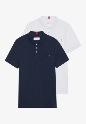 Two polo shirts: one navy blue and one white, both with a small red, white, and blue accent on the chest pocket and collar.