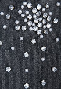 Tessuto nero con strass trasparenti sparsi e perle bianche di diverse dimensioni, disposti in un motivo decorativo. Texture complessivamente liscia.