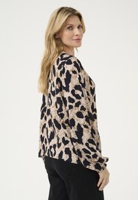Blouse à manches longues en imprimé léopard beige et noir. Tissu doux avec une coupe décontractée, dotée de poignets froncés et d'un ourlet arrondi.