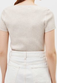 Jasnobeżowa prążkowana dzianinowa bluzka z krótkimi rękawami i szerokim dekoltem, zestawiona z białymi, wysokim stanem, postrzępionymi szortami z denimu.