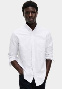 Weißes Hemd mit Knopfverschluss, einer Brusttasche, hochgekrempelten Ärmeln und einem klassischen Kragen. Der Stoff hat eine glatte und leichte Textur.