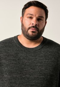 Tmavě šedý pletený svetřík s texturou obsahující jemné variace, kulatý výstřih a ribbované manžety. Bez viditelných vzorů nebo kovových doplňků.
