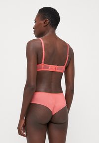 Ensemble de lingerie corail comprenant un soutien-gorge avec des bretelles réglables et une fermeture à crochet, ainsi que des culottes taille haute assorties avec des accents en dentelle.