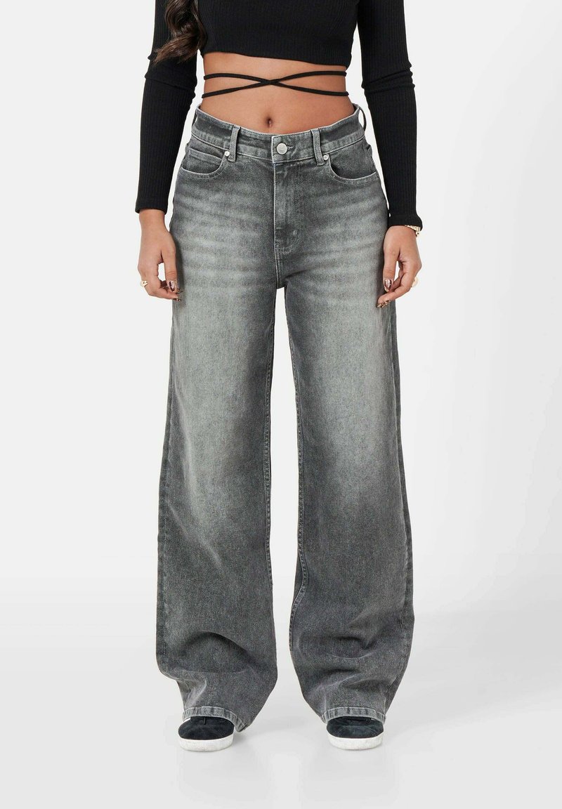 Jeans de pierna ancha en denim negro desteñido con cintura alta, cinco bolsillos y un ajuste relajado. Combinados con un top corto negro ajustado.