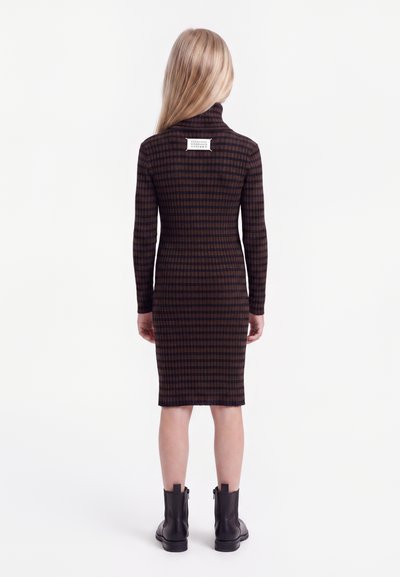 Fille aux longs cheveux blonds portant une robe à manches longues à carreaux marron et noir et des bottines noires, vue de dos.
