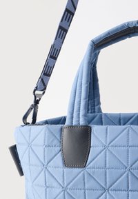 Γαλάζια καπιτονέ τσάντα χειρός με κοντά χερούλια, μαύρες δερμάτινες λεπτομέρειες και αποσπώμενο λουράκι ώμου με επωνυμία που στερεώνεται σε μεταλλικό κρίκο.