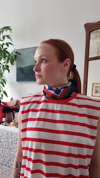 Rood-wit gestreepte mouwloze top met hoge hals, gelaagd met een kleurrijk patroon sjaal om de nek.