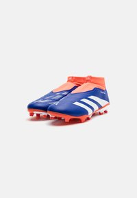 Botas de fútbol azules con acentos naranjas, collar tipo calcetín, superficie texturizada, rayas blancas y tapones cónicos para tracción en césped.