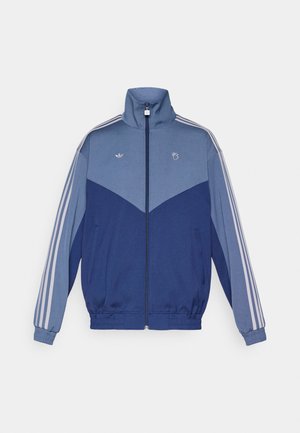 Chaqueta deportiva azul con un cuello alto, cierre de cremallera frontal y puños elásticos. Presenta un panel de un azul más claro y tres franjas blancas a lo largo de cada manga.