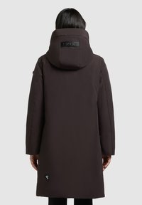Tumepruun pikk jakk kõrge krae ja kapuutsiga. Tagaküljel on logopatch ja see omab siledat, mattpinda.
