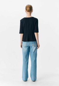 Zwarte top met korte mouwen en een ronde hals, met een lichte A-lijn snit, gecombineerd met lichtblauwe high-waisted jeans.