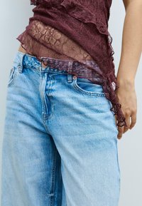 Burgundy spetsblus med volangkanter, lager på ljusblå denimjeans. Jeans har en avslappnad passform och klassiska framfickor.