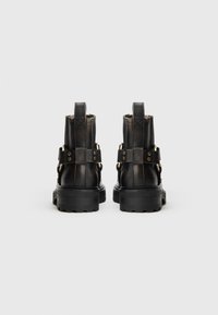 Botas de tobillo de cuero negro con suela rugosa, que cuentan con detalles en hardware dorado y correas ajustables en los laterales.