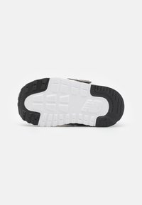Semelle de chaussure avec une semelle extérieure en caoutchouc noir à crampons profonds, une semelle intermédiaire blanche et une surface texturée pour l'adhérence et la stabilité.