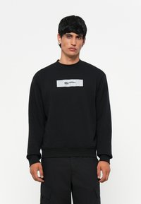 Čierna mikina z bavlneného zmesi, s okrúhlym výstrihom a rebrovanými manžetami. Uprostred bielej nášivky je text "KARL LAGERFELD JEANS".