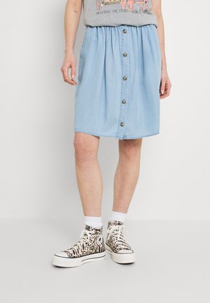 Jupe en chambray bleu clair avec taille élastique, boutons à l'avant et coupe décontractée. Associée à des baskets montantes noires et blanches à motif.
