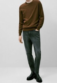 Maglione marrone lavorato a maglia con scollatura rotonda, abbinato a jeans grigi slim-fit e stivaletti neri alla caviglia. Texture liscia, design casual.