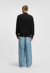 Oversized schwarzer Strickpullover mit Rundhalsausschnitt, kombiniert mit hellblauen weit geschnittenen Jeans. Der Stoff wirkt strukturiert und weich.