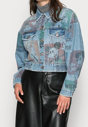 Denim jacket with colorful vintage Mickey Mouse comic prints worn over gray turtleneck and black leather pants.